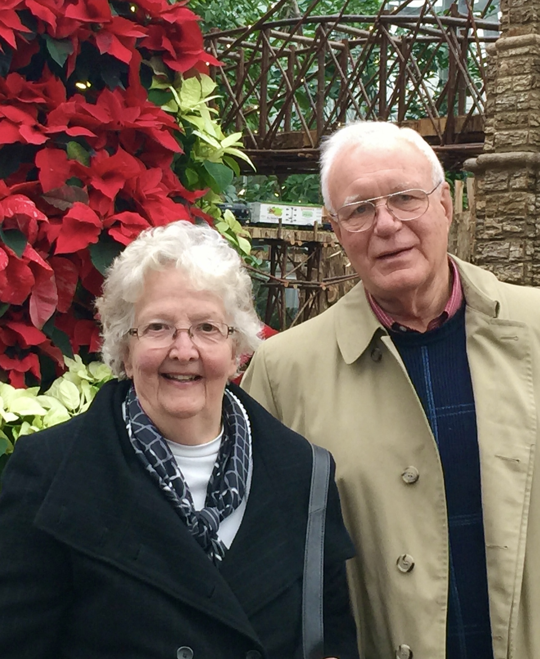 Nancy and George Bemis smiling in front of poinsettias.